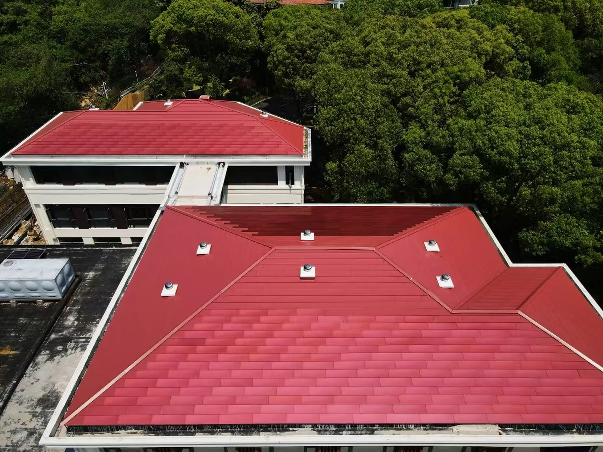 Close-up aerial view showing the precise integration of red solar tiles and ventilation systems on a complex roof structure.