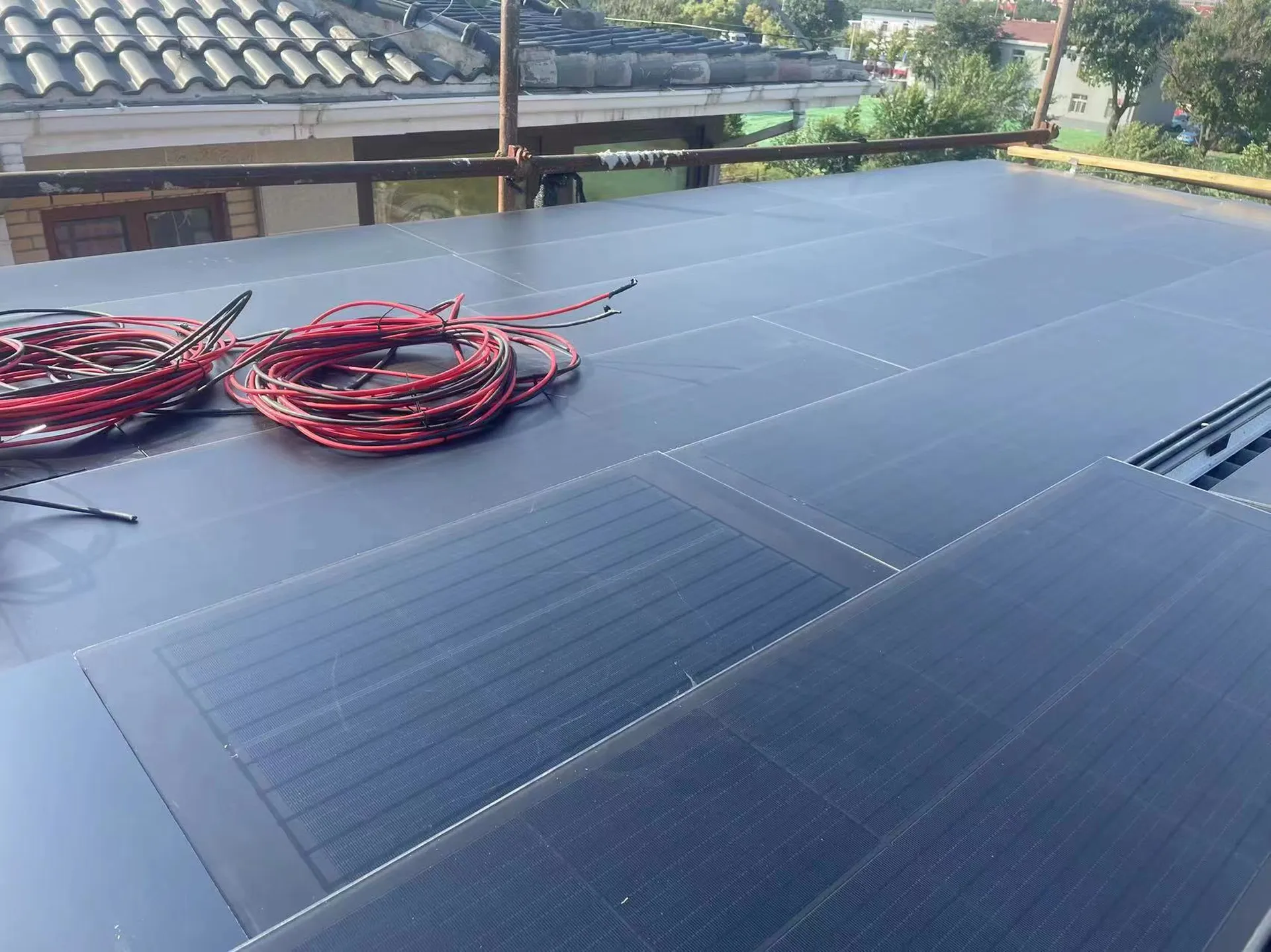 Red electrical cables laid across dark solar roof tiles during a residential installation.