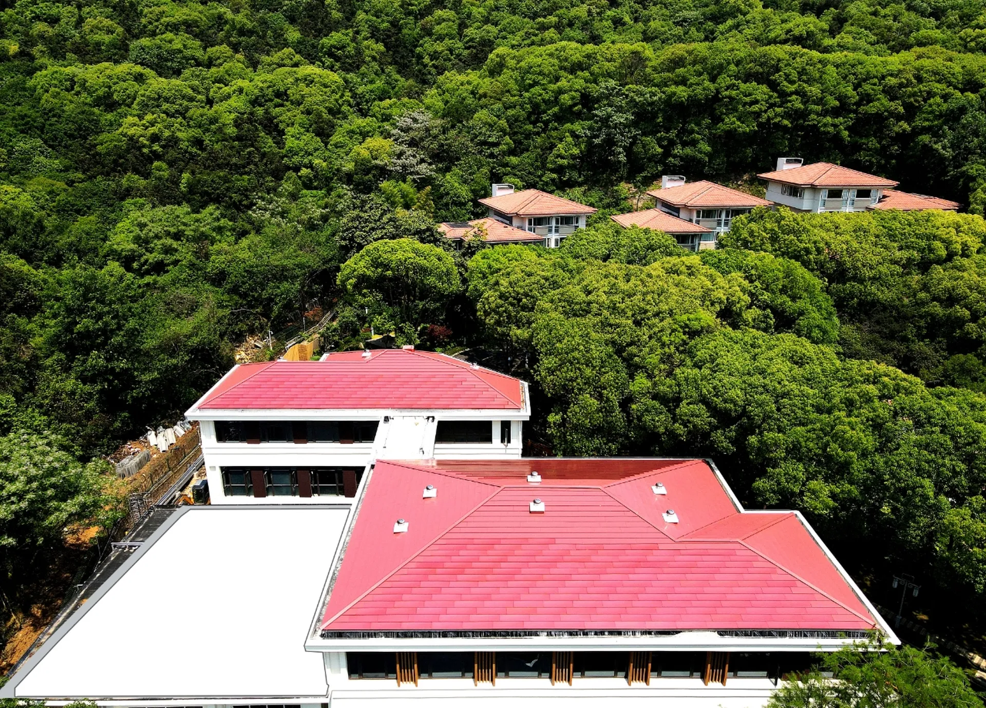 Wide aerial shot of a forest resort featuring vibrant red solar roofs that strictly respect traditional architectural aesthetics.