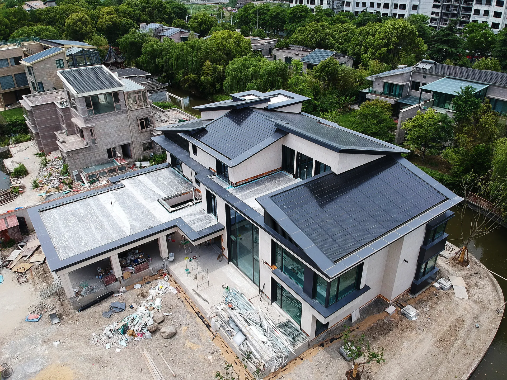 Aerial view of a custom luxury waterfront mansion featuring a seamlessly integrated, multi-tiered black BIPV roof.