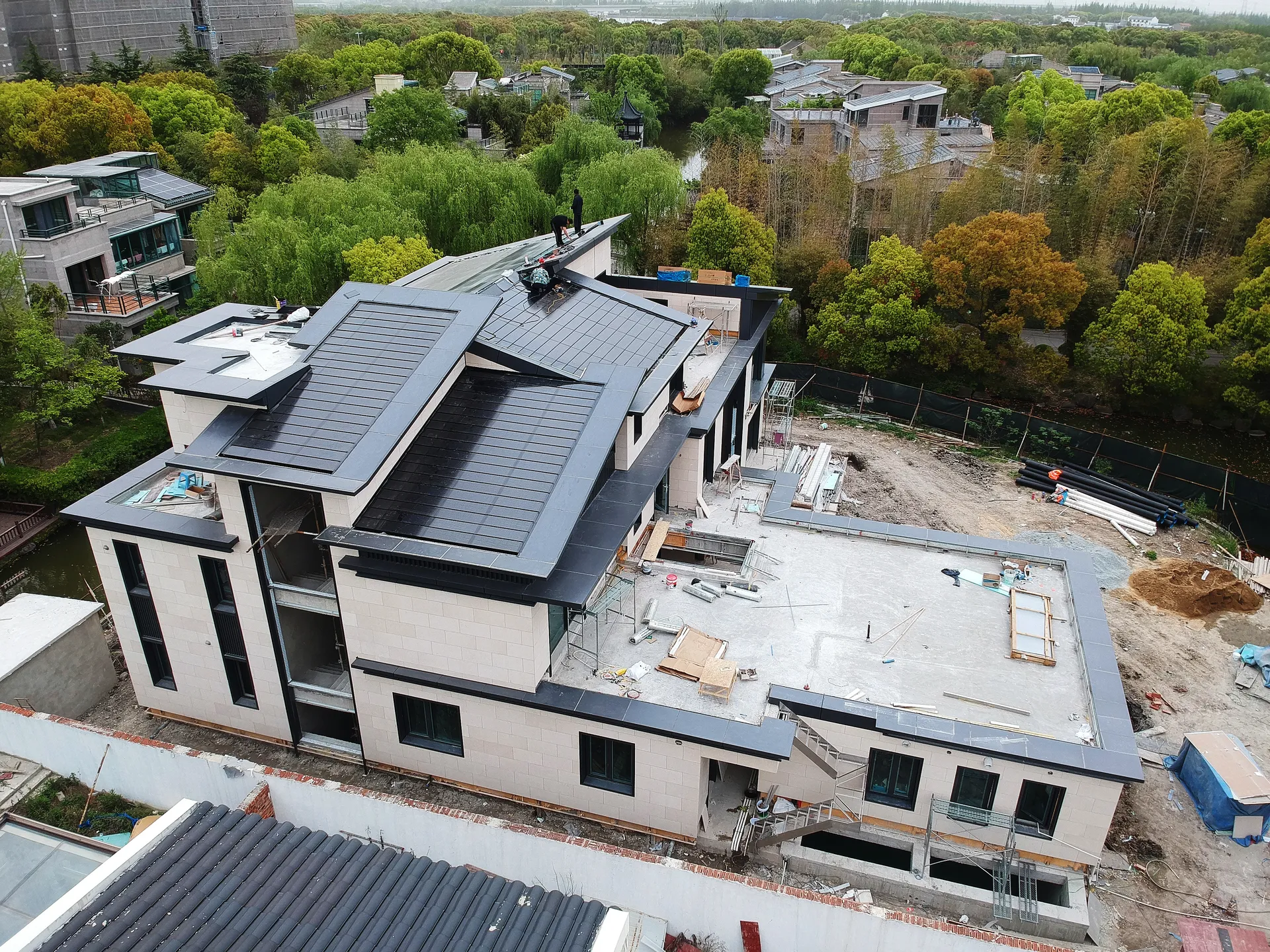 Workers fine-tuning the installation of solar tiles on a complex, multi-tiered luxury villa roofline.