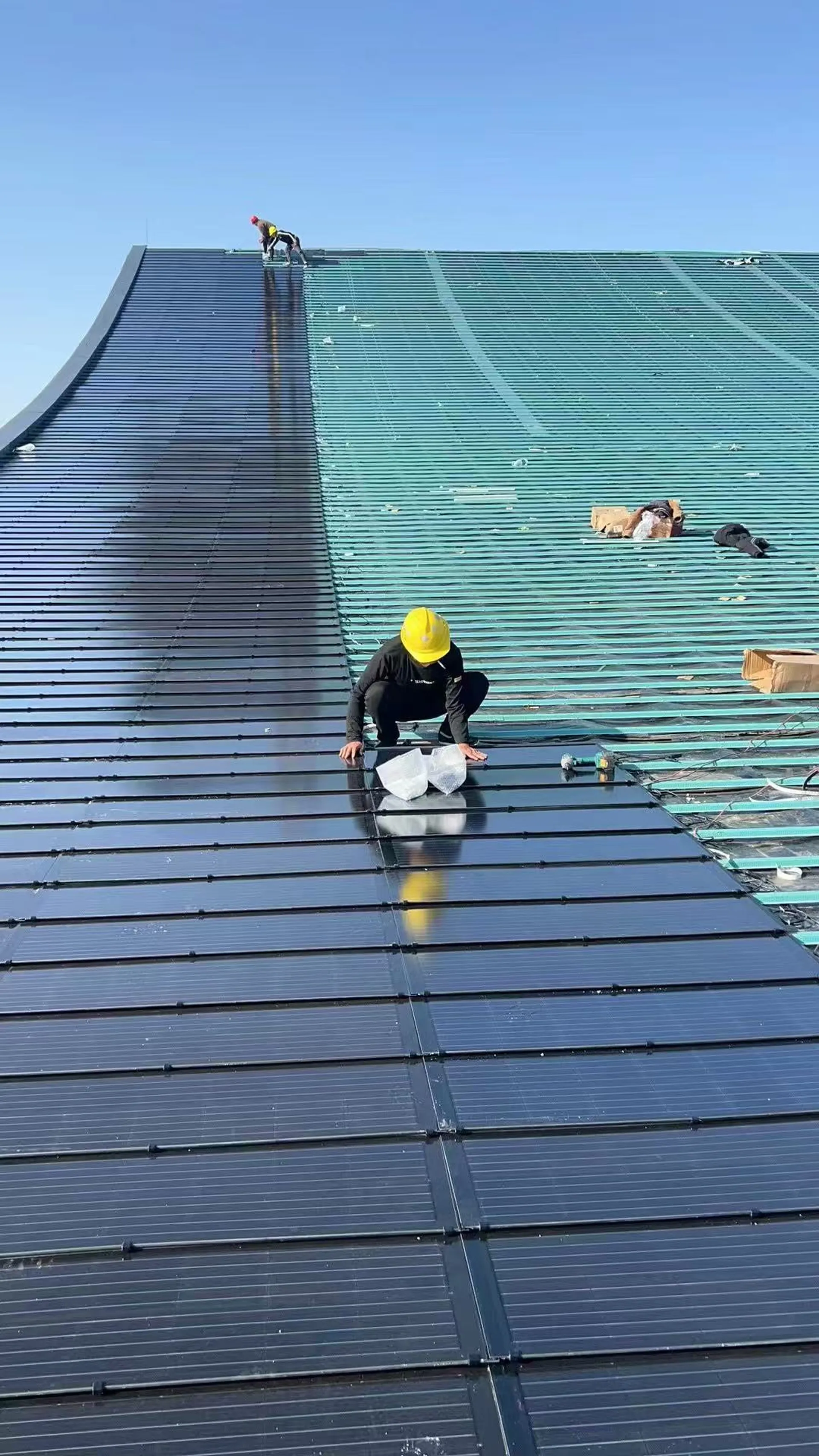 Worker installing dark solar roof tiles on a public facility roof.