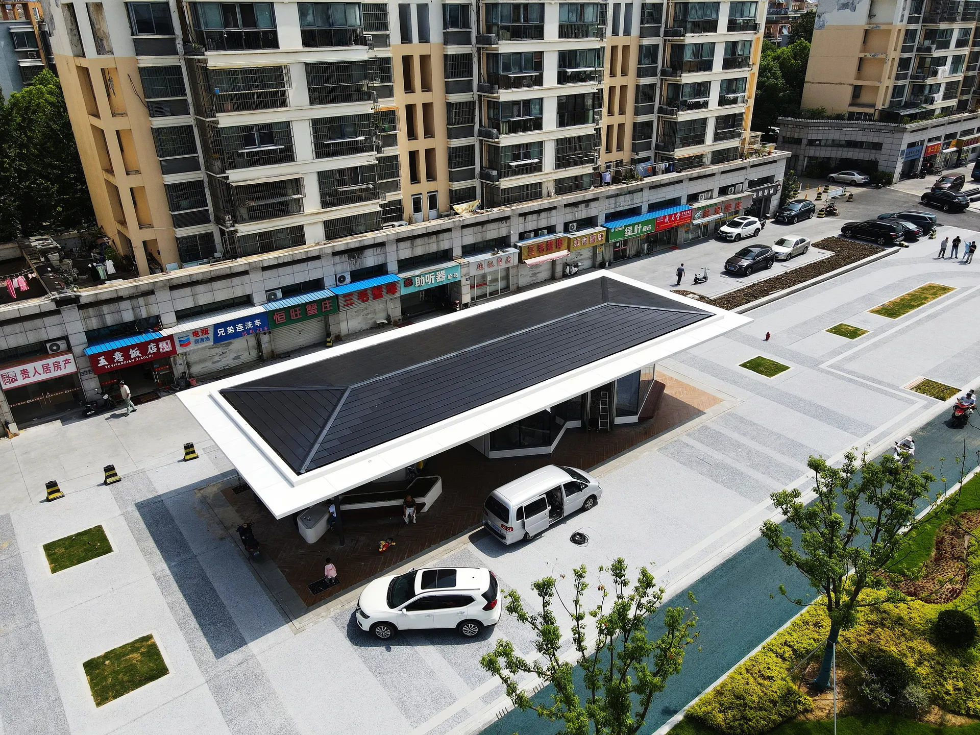 Angled aerial view of the smart city station, showing the seamless dark BIPV roofing contrasting with the white structural frame.
