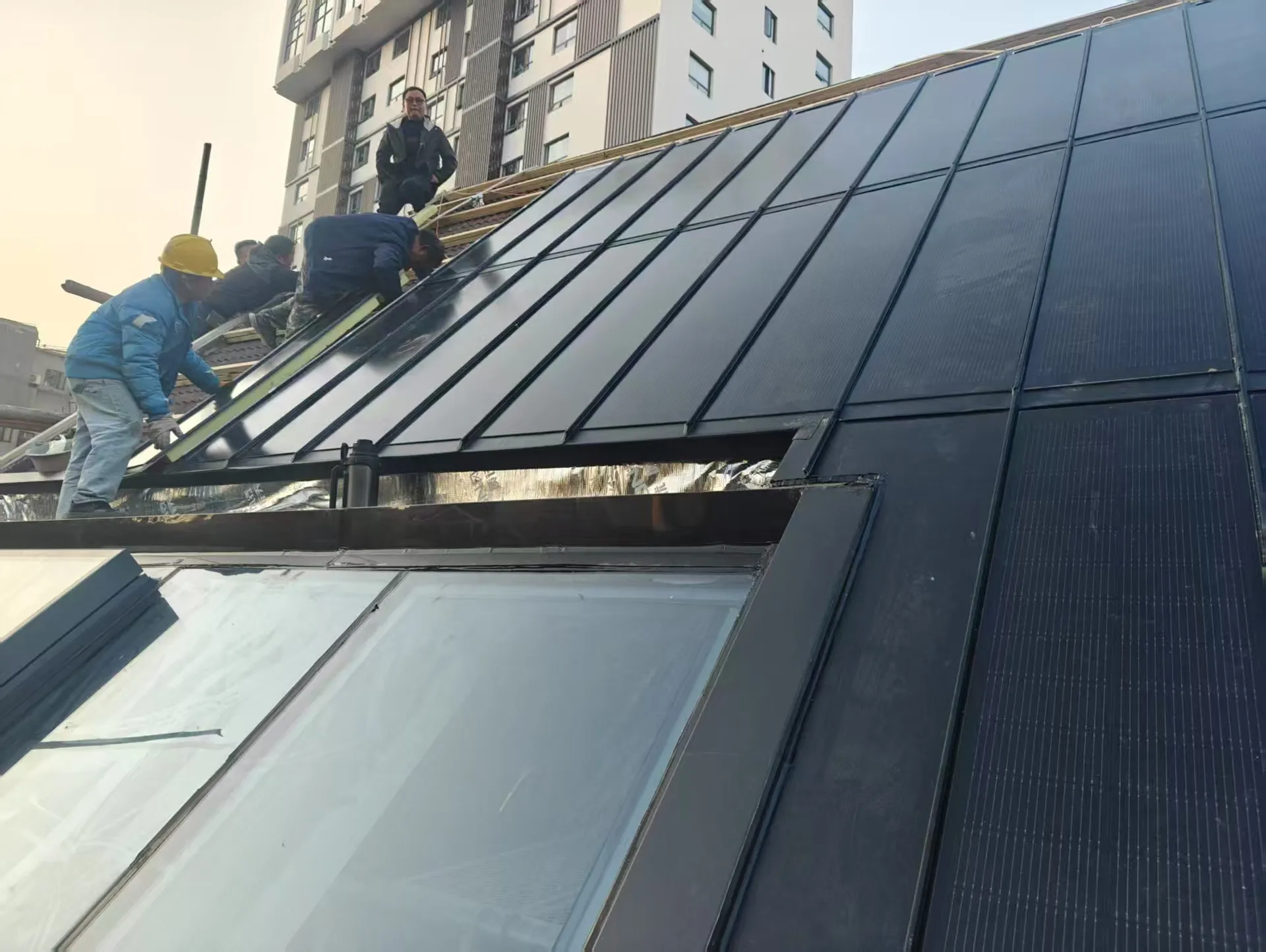 Workers installing heavy-duty Storm Guard BIPV panels on a compact urban residential roof.