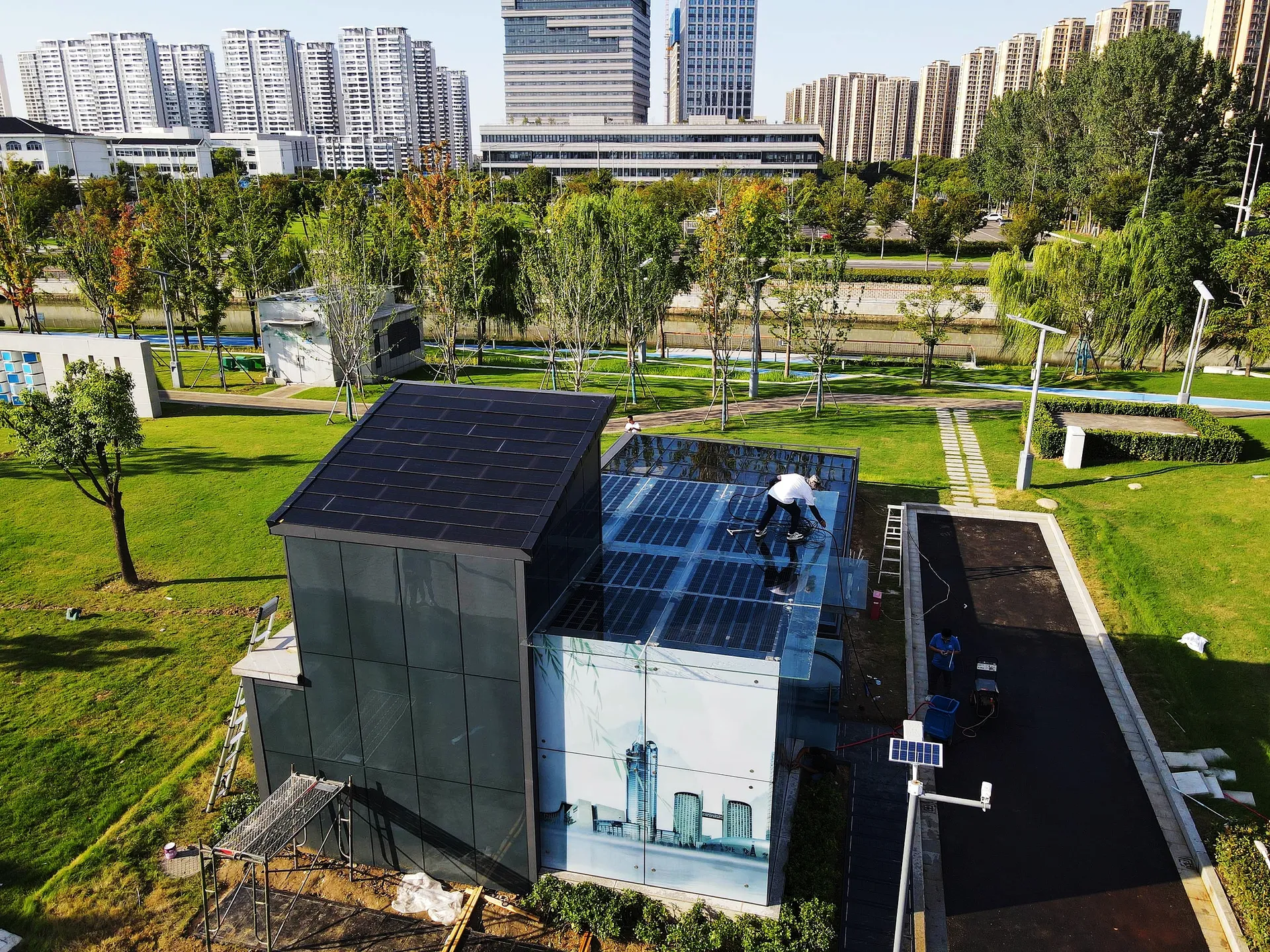 Worker cleaning the transparent solar glass canopy of a comprehensive BIPV demo station in an urban park.