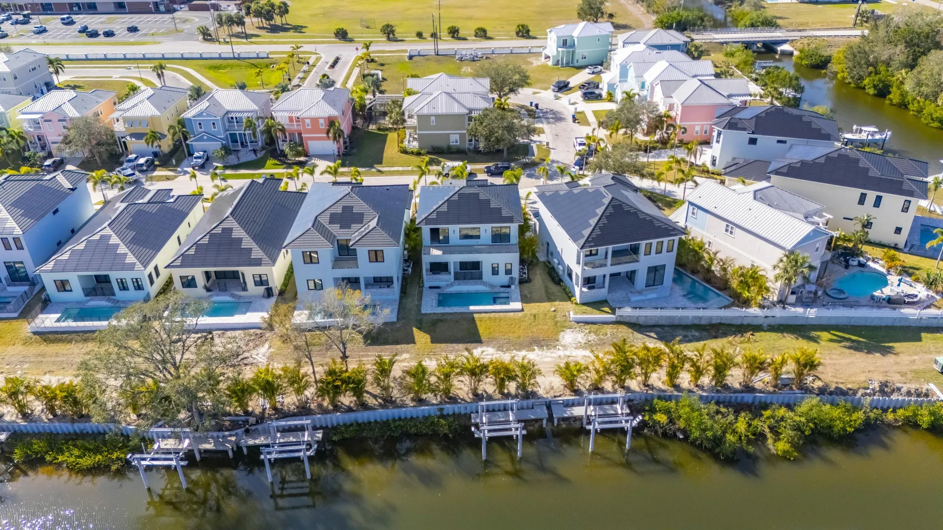 Waterfront aerial view showcasing a row of premium homes equipped with uniform, black solar tile roofs.