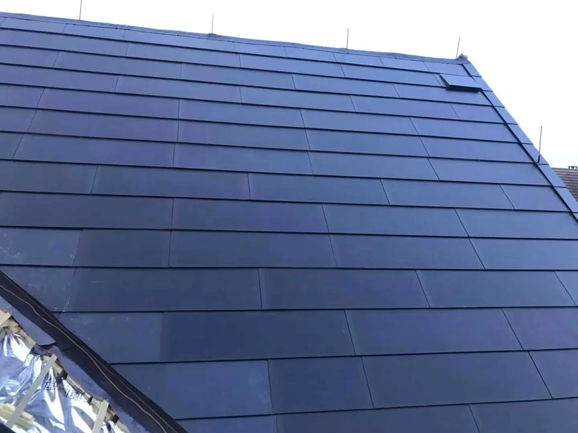 Expansive, sleek surface of the installed invisible solar tiles featuring a flawlessly integrated roof vent.