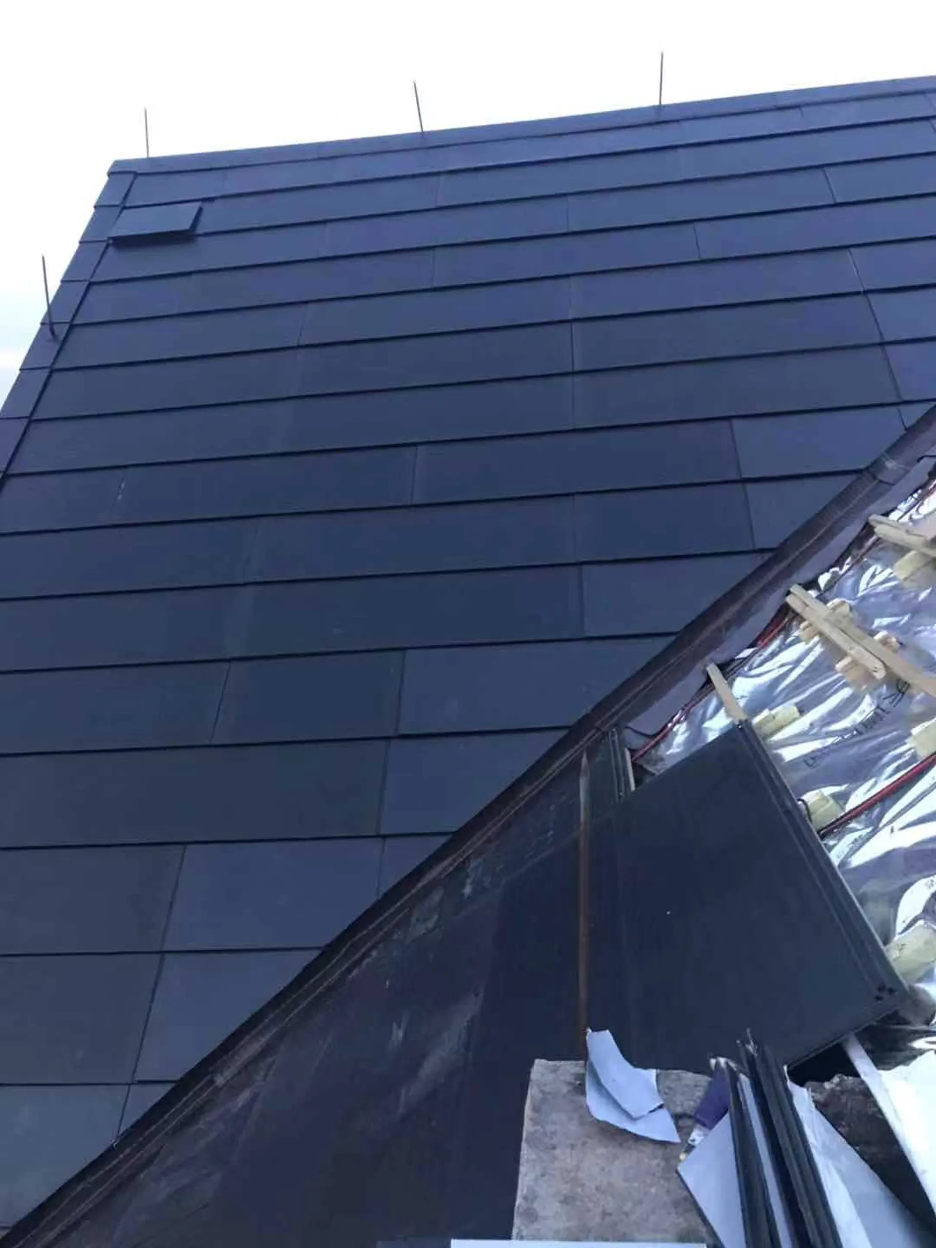 Close-up of the solar slate installation showing the underlying silver insulation layer and edge flashing process.